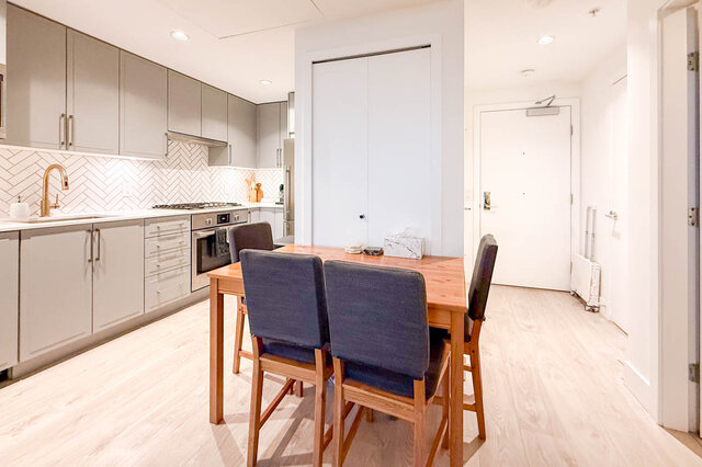Bright kitchen with white cabinets, herringbone backsplash, and hardwood floors. - 407-2435 Kingsway, Vancouver East Side