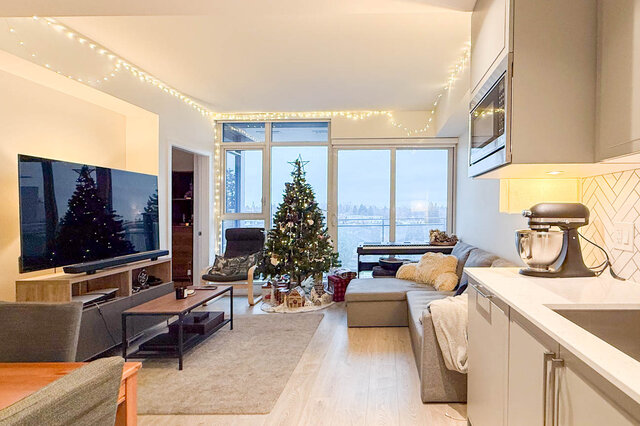 Spacious open-concept living room with hardwood floors, a festive Christmas tree, and a city view through large windows.