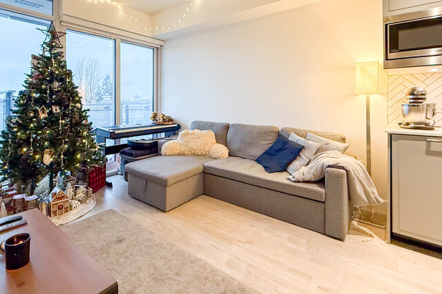 Cozy living room with hardwood floors, a festive Christmas tree, and a city view from the large window. - 407-2435 Kingsway, Vancouver East Side