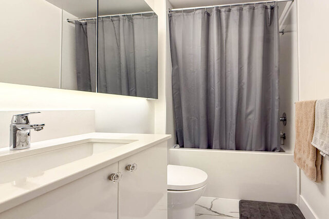 Modern bathroom with white countertop, gray shower curtain, and sleek fixtures. - 407-2435 Kingsway, Vancouver East Side