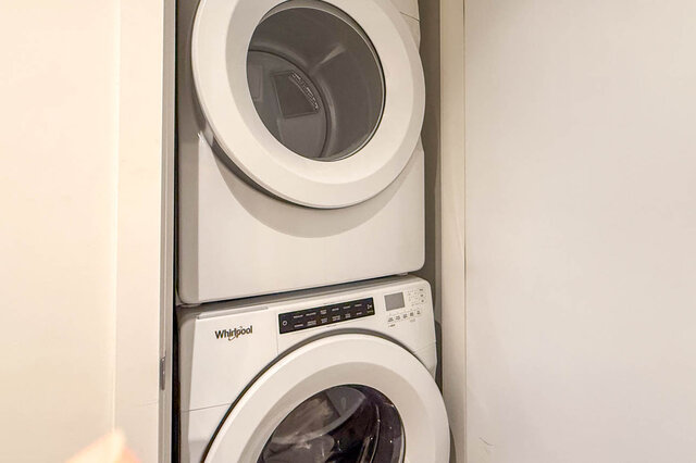 Bright laundry room with stacked washer and dryer, white walls, and modern design. - 407-2435 Kingsway, Vancouver East Side