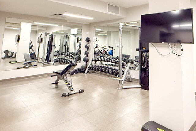 Spacious, well-equipped gym with mirrors, dumbbells, and a TV for workouts. - 407-2435 Kingsway, Vancouver East Side