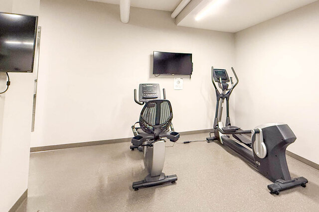 Spacious fitness room with cardio equipment and mounted TV, ideal for workout enthusiasts. - 407-2435 Kingsway, Vancouver East Side