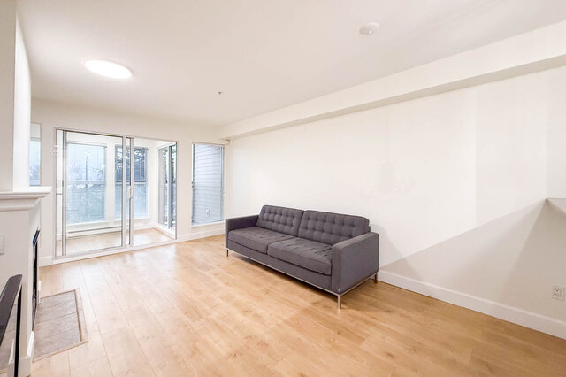 Spacious living room with hardwood floors, a modern grey sectional, and large windows offering a view. - 304-3637 West 17th Ave, Vancouver West Side