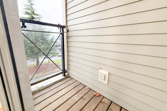 Balcony with wooden flooring and sliding glass door, offering a view of trees and a street. - 304-3637 West 17th Ave, Vancouver West Side