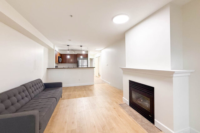 Spacious living room with hardwood floors, modern fireplace, and kitchen counter in the background. - 304-3637 West 17th Ave, Vancouver West Side