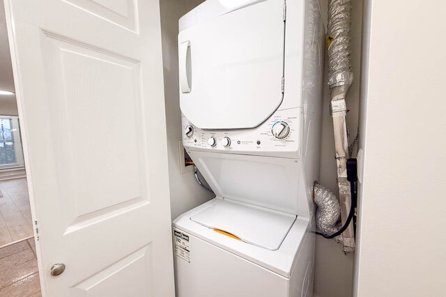 Compact laundry room with stacked washer and dryer, white door, and utility hose visible. - 304-3637 West 17th Ave, Vancouver West Side