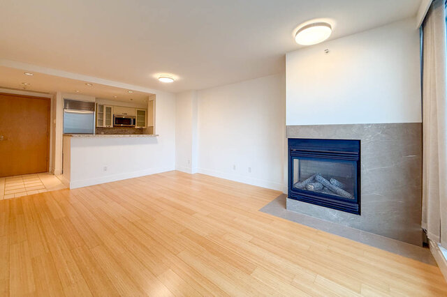 Open-concept living room with hardwood floors and a modern fireplace, leading to a kitchen with granite countertops.