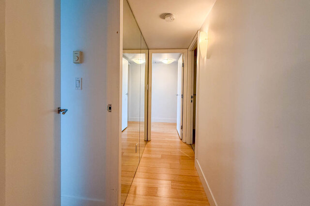 Spacious hallway with hardwood floors and modern light fixtures, leading to a bright, open-concept living area.