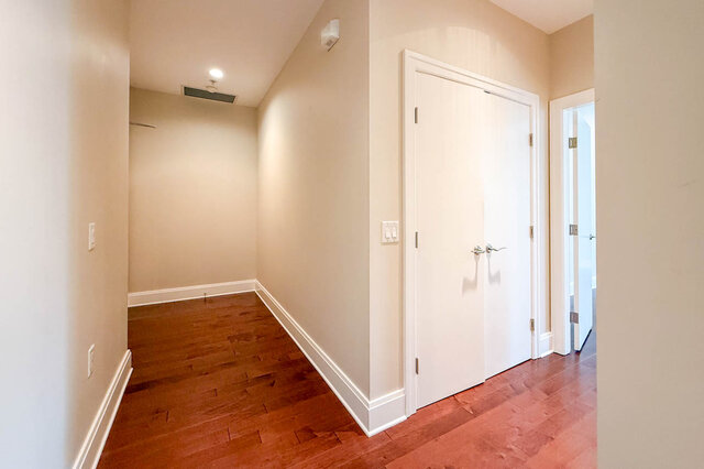 Spacious hallway with hardwood floors and white trim, leading to a door and a bright window. - 301-605 Clyde Ave, West Vancouver