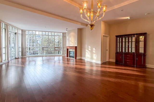 Spacious living room with hardwood floors, large windows, and a classic chandelier. - 301-605 Clyde Ave, West Vancouver
