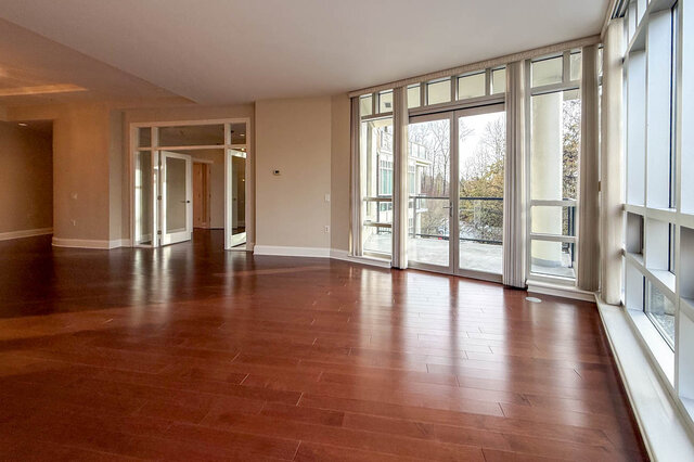 Spacious living room with hardwood floors and large windows, offering a serene outdoor view. - 301-605 Clyde Ave, West Vancouver