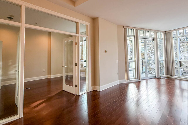 Spacious living room with hardwood floors and large windows offering a city view. - 301-605 Clyde Ave, West Vancouver