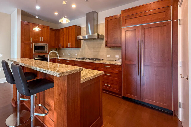 Modern kitchen with granite countertops, wooden cabinets, and stainless steel appliances. - 301-605 Clyde Ave, West Vancouver