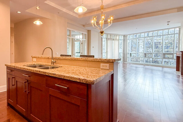 Spacious kitchen with granite countertops and hardwood floors, featuring a large island and city view. - 301-605 Clyde Ave, West Vancouver