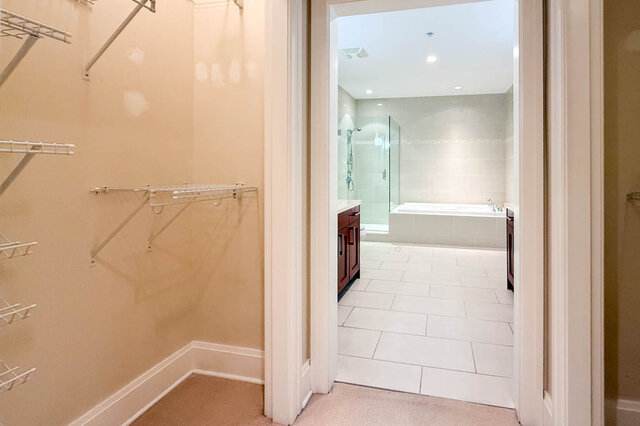 Spacious walk-in closet with built-in shelves and a view into the modern bathroom with a glass-enclosed shower and bathtub.