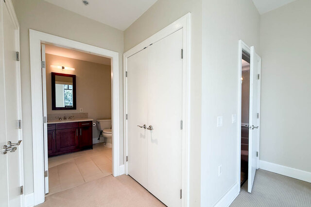 Spacious bedroom with a walk-in closet and a bathroom featuring a dark vanity and a large mirror. - 301-605 Clyde Ave, West Vancouver