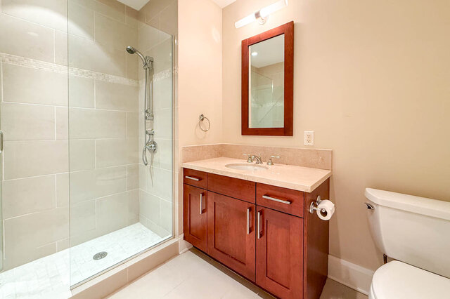 Spacious bathroom with marble countertops, wooden cabinets, and a walk-in shower. - 301-605 Clyde Ave, West Vancouver