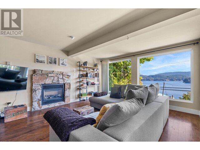 Spacious living room with a stone fireplace, hardwood floors, and a stunning view of the water. - 2621 Panorama Drive, North Vancouver