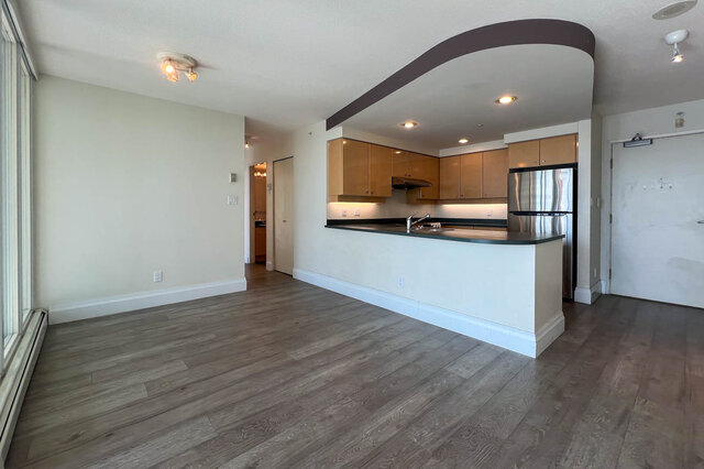 Open-concept living space with hardwood floors and a modern kitchen featuring a black countertop and stainless steel...