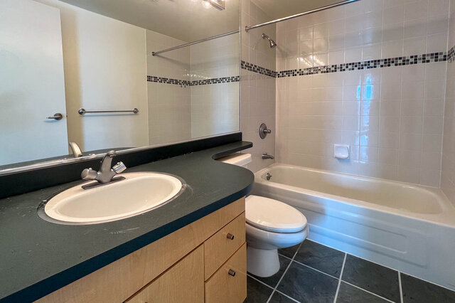 Modern bathroom with a large vanity, black countertop, and a bathtub with a shower. - 2905-1009 Expo Boulevard, Vancouver Downtown