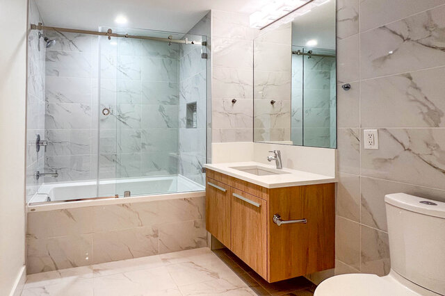 Modern bathroom with marble tile walls and wood vanity sink. - 309-2738 Library Lane, North Vancouver