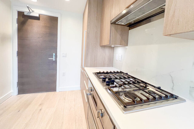 Kitchen with white quartz countertops and stainless steel gas stove in modern condo unit. - 309-2738 Library Lane, North Vancouver