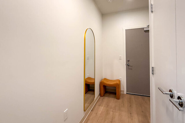 Entryway with light hardwood floors, a gold-framed arched mirror, and a mustard-orange bench. - 115-1529 Oxford Street, North Vancouver