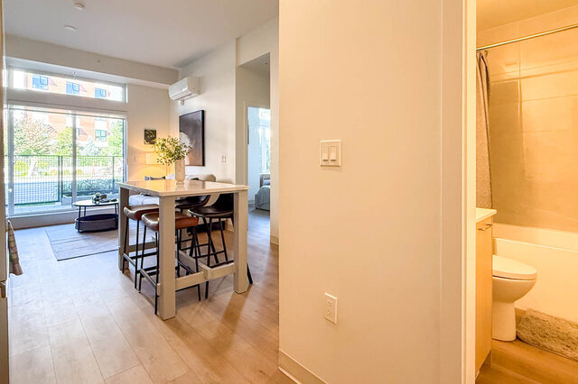 Dining area with white table and leather bar stools on hardwood floors, plus a bathroom and balcony access. - 115-1529 Oxford Street, North Vancouver