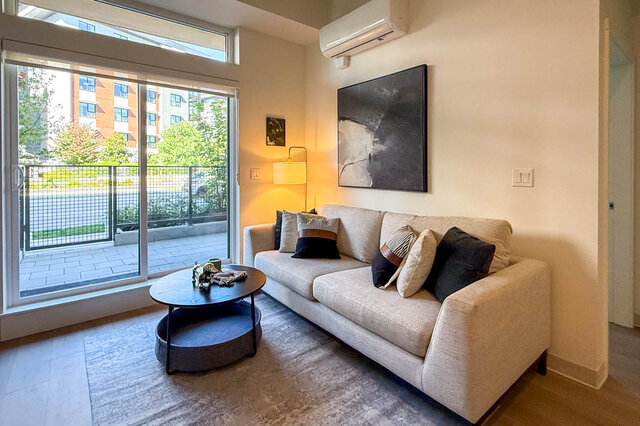 Furnished living room with a cream sofa, round coffee table, and sliding glass doors opening to a balcony. - 115-1529 Oxford Street, North Vancouver