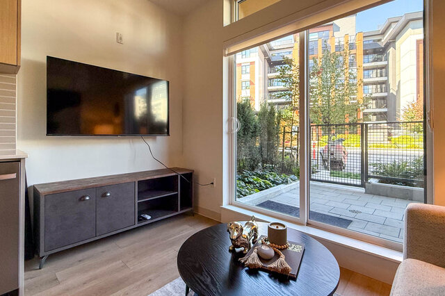 Living room with hardwood floors, wall-mounted TV, and a large sliding door opening to a balcony with courtyard views.