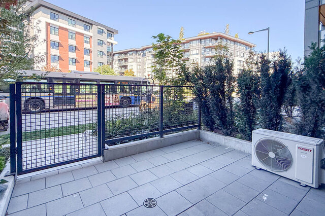 Tiled balcony with black metal railing, outdoor AC unit, and a view of the street and surrounding buildings. - 115-1529 Oxford Street, North Vancouver