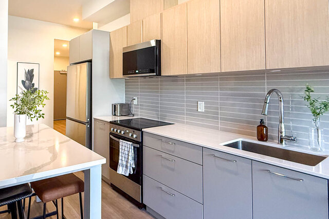 Modern kitchen with white countertops, grey cabinetry, and a breakfast island. - 115-1529 Oxford Street, North Vancouver