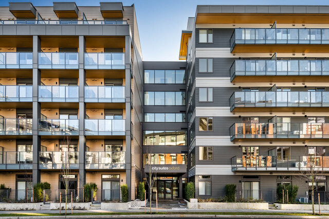 Modern condo exterior featuring glass-railed balconies and a gray-and-wood facade with a central glass entry.