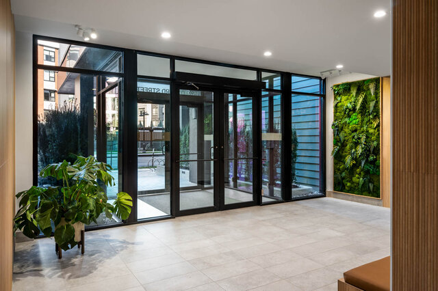 Spacious entryway with light tile floors, floor-to-ceiling glass doors, and a lush vertical green wall. - 115-1529 Oxford Street, North Vancouver