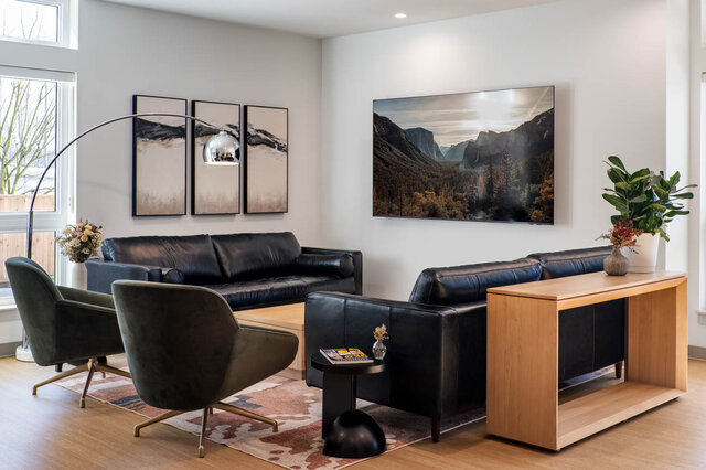 Furnished living room with black leather sofas, olive velvet chairs, and light hardwood floors. - 115-1529 Oxford Street, North Vancouver