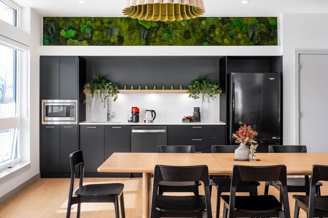 Modern kitchen and dining area with dark cabinetry, white countertops, hardwood floors, and a living green wall.
