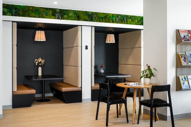 Dining nook with tan booth seating, black pendant lights, a moss wall accent, and light hardwood floors. - 115-1529 Oxford Street, North Vancouver