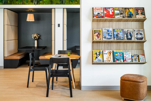 Dining nook with a round wooden table, black chairs, and a wall-mounted magazine rack on light hardwood floors.