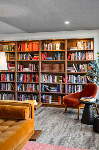 Furnished living room featuring floor-to-ceiling wooden bookshelves and a tufted amber sofa. - 115-1529 Oxford Street, North Vancouver