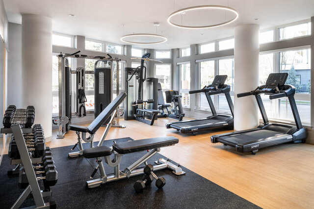 Modern fitness room with hardwood floors, large windows, and Spirit treadmills and free weights. - 115-1529 Oxford Street, North Vancouver