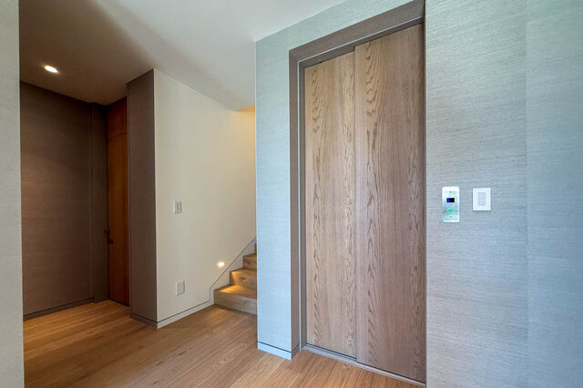 Modern elevator hallway with wood-veneer doors and hardwood flooring. - 2390 Westhill Drive, West Vancouver