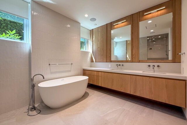 Bathroom with freestanding white tub and wooden vanity, large windows overlooking greenery. - 2390 Westhill Drive, West Vancouver