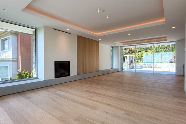 Spacious living room with hardwood floors and modern fireplace, large windows overlooking greenery. - 2390 Westhill Drive, West Vancouver