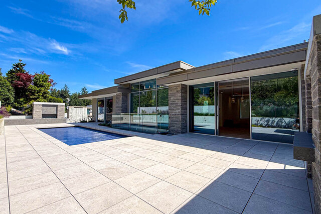 The pool area features a swimming pool, large glass windows, stone columns, and tiled patio. - 2390 Westhill Drive, West Vancouver