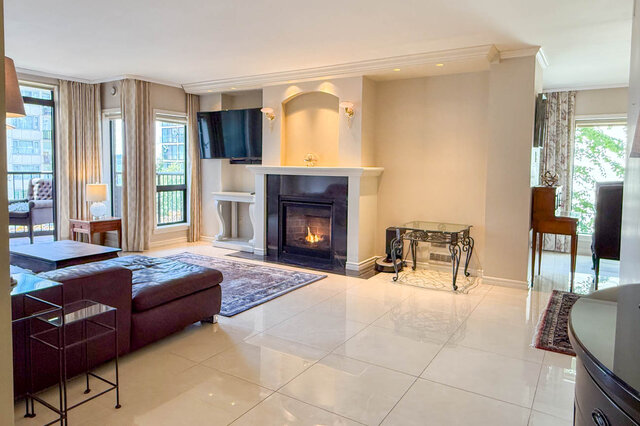 Spacious living room with lit fireplace, white tile floors, and city views through tall windows. - 302-1520 Harwood Street, Vancouver Downtown