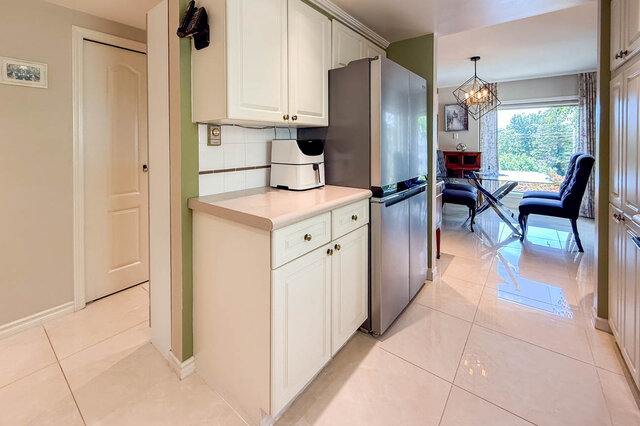 Bright kitchen with white cabinetry, stainless steel fridge, and sunlit view into dining space. - 302-1520 Harwood Street, Vancouver Downtown
