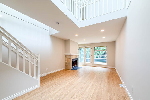Spacious living room with hardwood floors and a stone fireplace beneath high ceilings. - 3443 West 6th Ave, Vancouver West Side