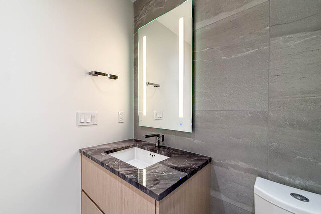 Modern bathroom with dark marble countertop and illuminated mirror. - 406-777 Harbour Way, North Vancouver