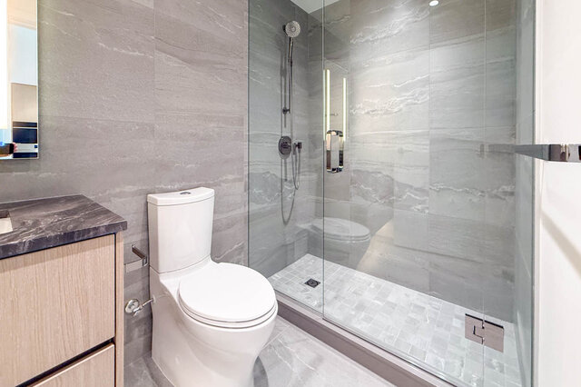 Modern bathroom with marble tile walls and glass-enclosed shower. - 406-777 Harbour Way, North Vancouver